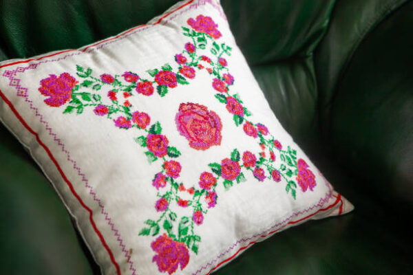 Handmade decorative pillow with rose embroidery on a green leather sofa.