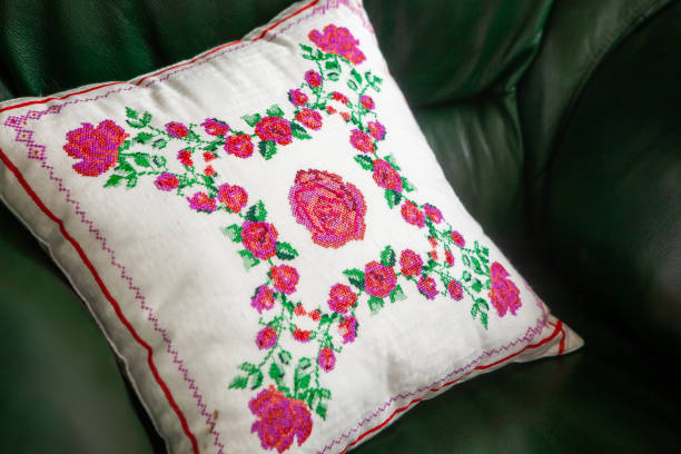 Handmade decorative pillow with rose embroidery on a green leather sofa.